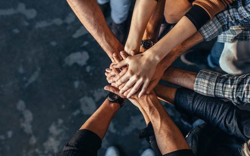 Top view of creative professionals putting their hands together as a symbol of teamwork, cooperation and unity. Stack of hands of men and woman.